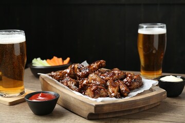 Tasty chicken wings, sauces, vegetable sticks and glasses of beer on wooden table, space for text. Delicious snacks