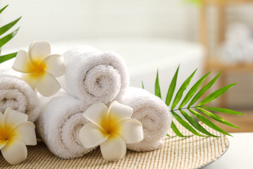Spa composition. Towels, plumeria flowers and palm leaves on table indoors, closeup