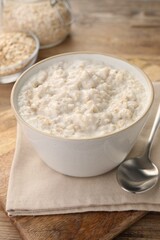 Tasty boiled oatmeal in bowl and spoon on wooden table