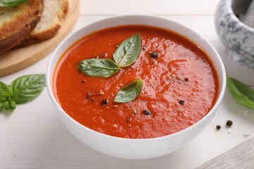 Delicious tomato cream soup in bowl on white wooden table, closeup