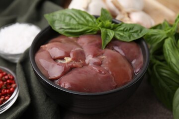 Bowl of raw chicken liver with basil on grey table, closeup