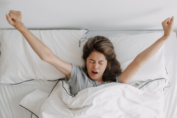 Top view of yawning and stretching asian woman just wake up on the bed. - obrazy, fototapety, plakaty