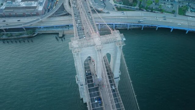 Top down aerial cars driving by Brooklyn Bridge above blue East River. Traffic highway transportation at Manhattan in New York downtown. Scenic Brooklyn Bridge towers architecture with American flag