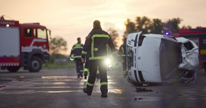Brave Firefighters Team Walking to the Camera. In Background Paramedics and Firemen Rescue Team Fight Fire in Car Accident, Insurance and Save Peoples Lives concept.
