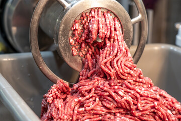 Close-up view of a meat grinder grinding Hamburger or Sausage Meat. - obrazy, fototapety, plakaty