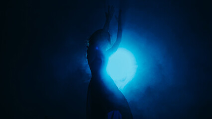 Choreography performance. Dancer show. Professional artistic woman moving in blue mist shadow in bright projector light on dark background copy space.