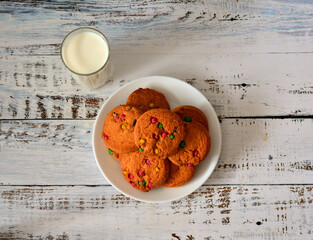 A white plate with several fresh oatmeal cookies and a glass of hot milk on a light wooden table.