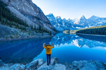  female backpacker travels and hikes to the top of a mountain, standing and admiring the view of Moraine lake in Banff National park. - obrazy, fototapety, plakaty