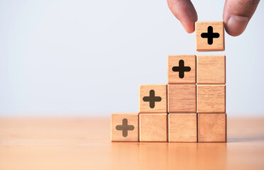 Hand stacking increasing of plus sign on wooden block cube for value added concept.