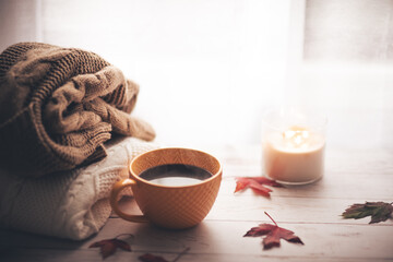 Cup of coffee in autumn, candle and knit warm sweaters on the background.Cozy home