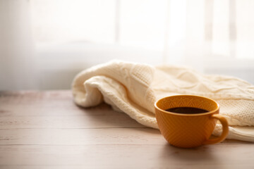 Yellow cup of coffee in autumn and knit warm sweater on the background. Copy space for text. Cozy home