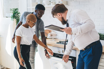 Confident estate agent showing kitchen to African American thoughtful couple