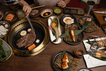A set of grill food on a wooden table in restaurant.Fresh meat and shrim sliced for grilled menu.Party of friends or family eating dinner on wooden table background.