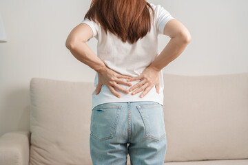 woman having back body ache during sitting on Couch at home. adult female with muscle pain due to Piriformis Syndrome, Low Back Pain and Spinal Compression. Office syndrome and medical concept - obrazy, fototapety, plakaty