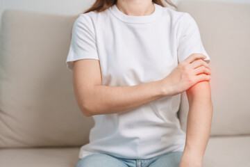 Woman having arm pain during sitting on couch at home, muscle injury and ache. Health and medical concept