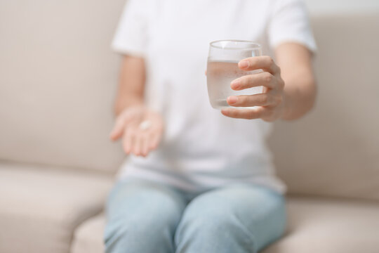 woman hand holding medicine painkiller pill and water glass on the sofa at home, taking for headaches,  stomach ache, Diarrhea Pain from food poisoning, Endometriosis, Hysterectomy and Menstrual