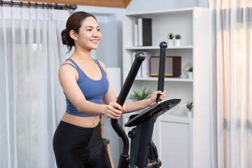 Energetic and strong athletic asian woman running on elliptical running machine at home. Pursuit of...