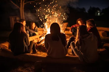 Fotobehang Group of young friends sitting near bonfire at night. Camping concept, Friends sitting in front of a bonfire, top section cropped, no visible faces, AI Generated © Ifti Digital