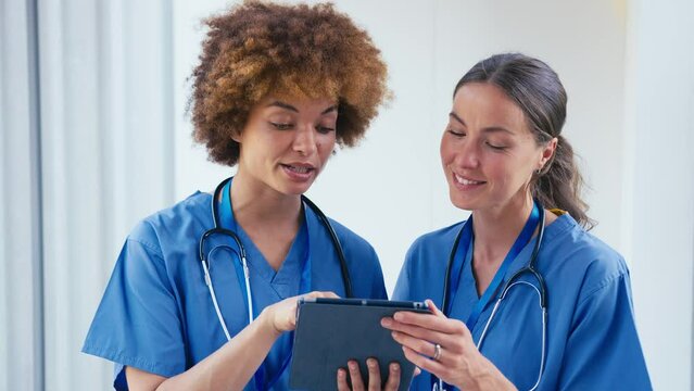 Close up of two female doctors wearing scrubs with digital tablet discussing patient notes in hospital - shot in slow motion