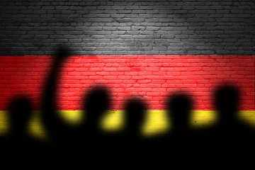 Poster The refugees migrate to Germany . Silhouette of illegal immigrants . Europe union migration policy. Germany flag painted on a brick wall with protesters © Tomas Ragina