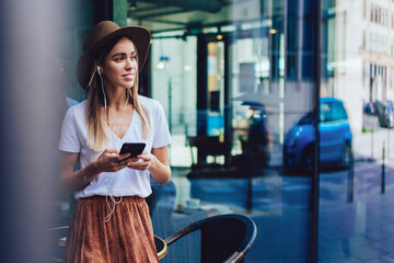 Pensive female in earphones with smartphone on street