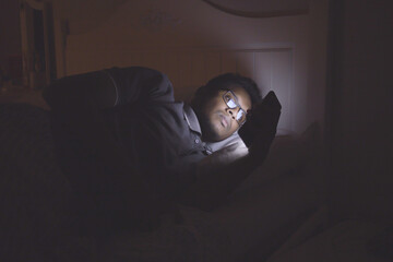 young man sitting on bed using smart phone at night 