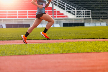 Fototapeta premium The feet of an athlete running outdoors at the racetrack. Fit young man is running on the race track. Male runner in sportswear running on stadium track with red coating outdoors.