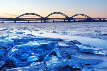 close-up of broken ice on the river and beautiful bridge at sunset