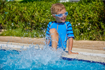 Summer swimming and rest of a little smiling blond boy in a blue bathing suit in the pool. Happy...