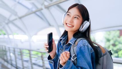 Portrait of happy young asian woman listening music online with wireless headphones from a smartphone in the city - obrazy, fototapety, plakaty