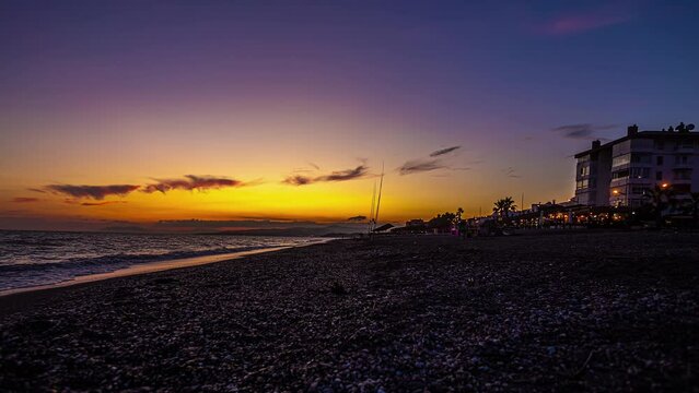 Fishermen and people relax on Playa de Torrox Malaga Spain, sunset glow spreads in sky