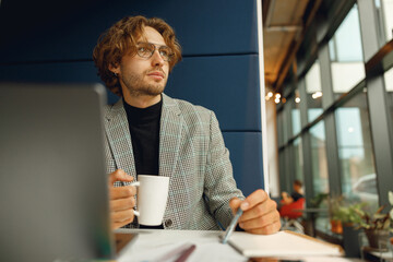 Focused businessman working on project while using laptop and making notes while sittting in office