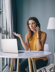 Enthusiastic female sitting at table with documents and notebook chatting by mobile