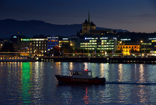Geneva, Switzerland, Europe - Night view of city center with historic facades on shore of Lake Geneva, colorful neons of watch and jewellery producers, St Pierre Cathedral on the hill
