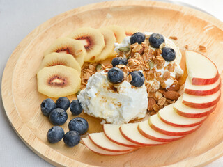 Fresh fruit and granola with yogurt in wooden plate.