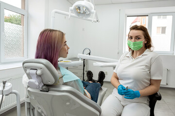 patient sitting dental chair next to female dentist doctor who is conducting an examination.