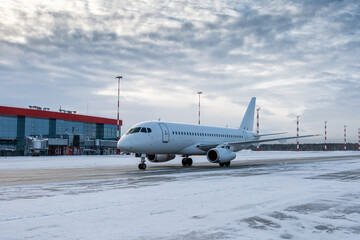 White passenger airplane taxiing on the airport apron at winter