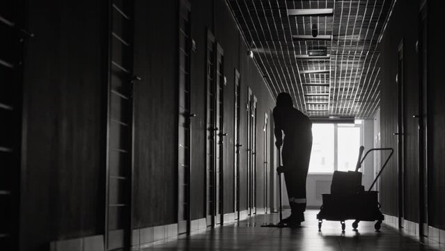 Monochromatic silhouette of janitor with trolley mopping floors in hospital