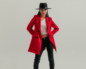 cool fashion girl with hat in red coat holding hands behind and posing