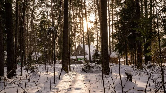small wooden house in a snow-covered winter forest. slow horizontal movement of the camera. The sun's rays break through the trees