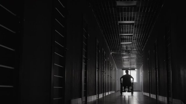 Monochromatic long shot of wheelchair user going through dark hallway