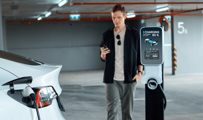 Young man travel with EV electric car to shopping center parking lot charging in downtown city...