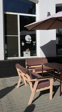 pizzeria with outdoor tables and sun umbrellas standing near the window with inscriptions in Russian "coffee" and "pizza", street lunch area in a town on a sunny day