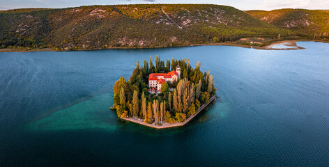 Visovac, Croatia - Aerial panoramic view of Visovac Christian monastery island in Krka National Park on a sunny autumn morning with golden sunrise, colorful autumn foliage and clear turquoise water