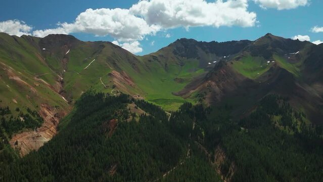 Aerial cinematic drone summer high altitude Silverton Mountain Ski Resort southern Colorado blue sky late morning stunning lush green blue sky partly cloudy Rocky Mountains forward reveal motion