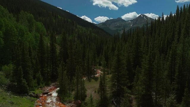 Aerial cinematic drone orange river Cement Creek summer high altitude downtown Silverton Telluride Prospect Gulch Colorado Rocky Mountains stunning drive looking up steam backward movement