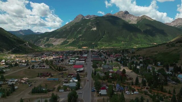 Aerial cinematic drone summer morning downtown Silverton Main Street southern Colorado Red Mountain Pass stunning lush green blue sky partly cloudy Rocky Mountains town clouds forward movement