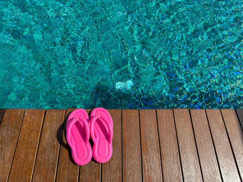 Clear rippled water in swimming pool and pink flip-flops on wooden deck outdoors, above view. Space for text