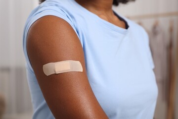 Young woman with adhesive bandage on her arm after vaccination indoors, closeup - obrazy, fototapety, plakaty