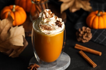 Glass of pumpkin spice latte with whipped cream and ingredients on black table, closeup